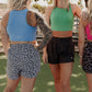 3 blonde haired women standing in the middle of a tennis court.  some of them are facing forward and some back wards.  they are all wearing 3 different long lined tank top and 3 different printed running shorts in snow leopard, grey leopard and panther.