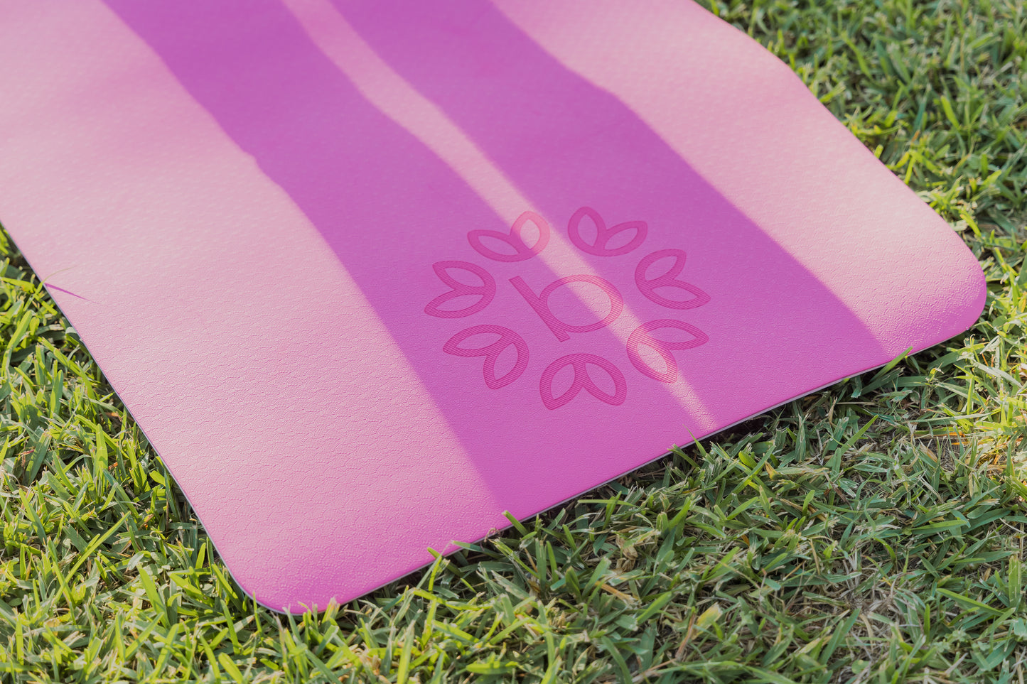 picture of a pink yoga mat that is laying on green grass.