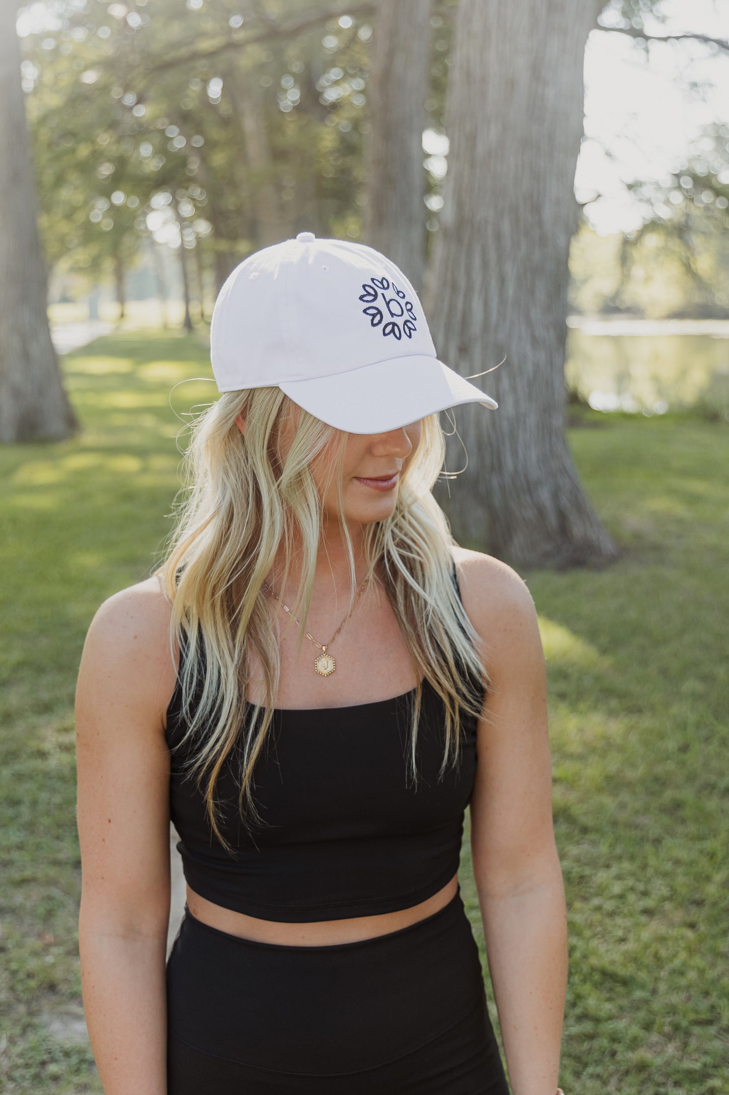 White women with blonde hair wearing a white baseball cap with a logo on the front of it.