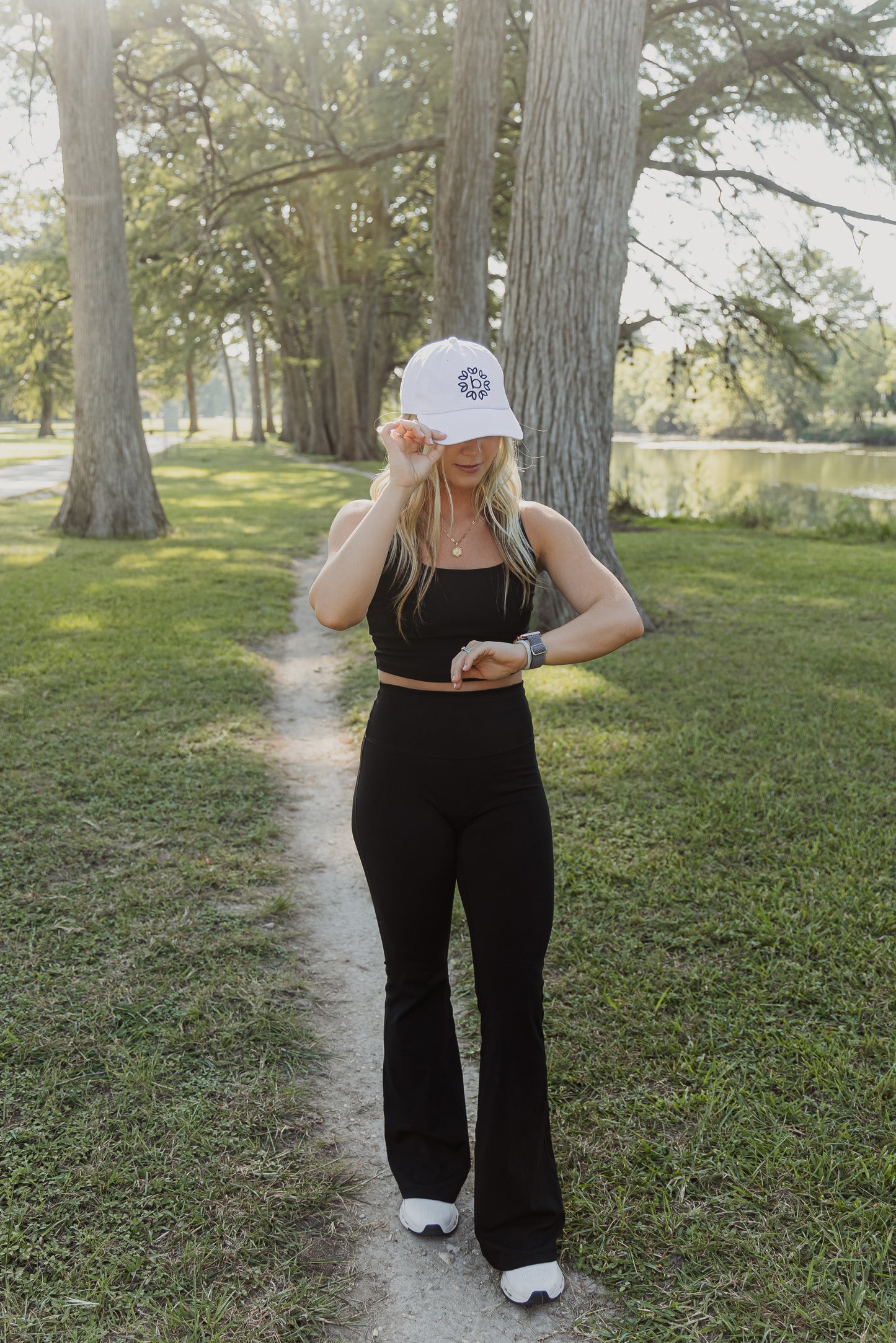 White women with blonde hair wearing a white baseball cap with a logo on the front of it.