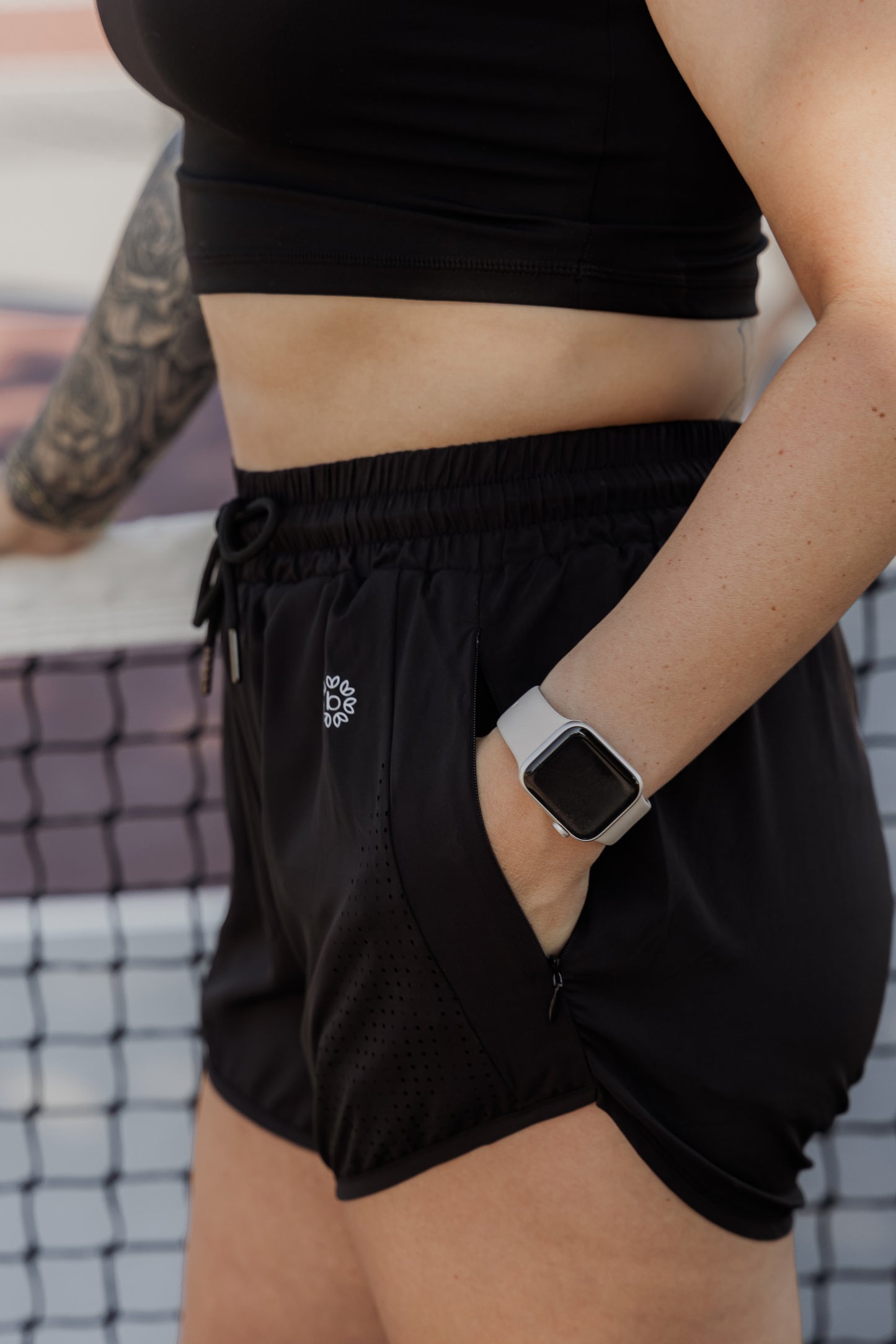 White women wearing a pair of black running shorts. She is showing off that the black running shorts has pockets. It only shows some of her arm and the shorts.