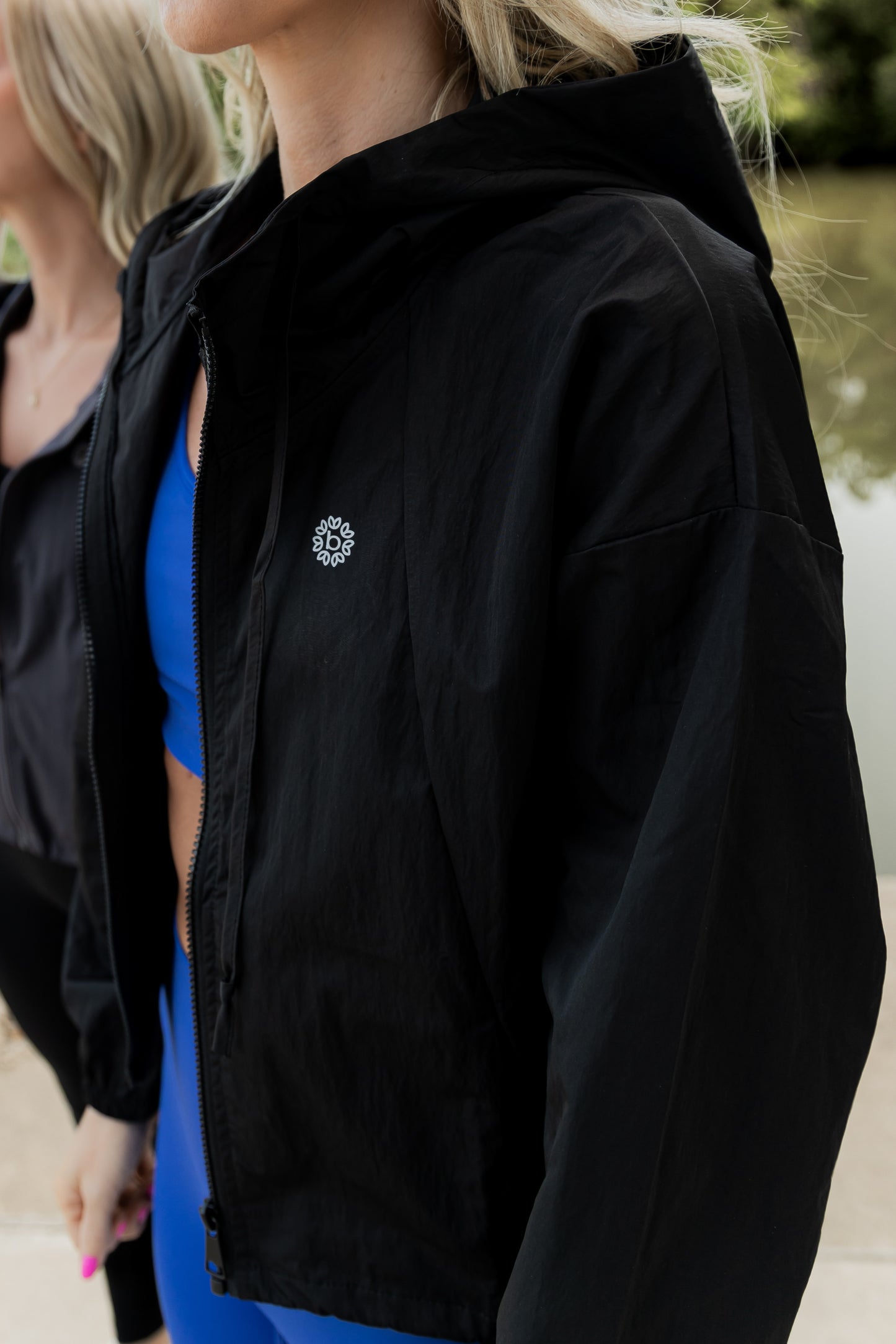 White women with blonde hair wearing a black cropped hooded wind/rain jacket.