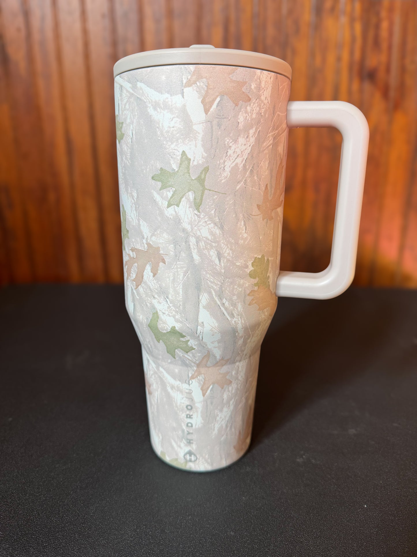 HydroJug 40 oz tumbler in the color camo. Sitting on a black shelf with a wood background.