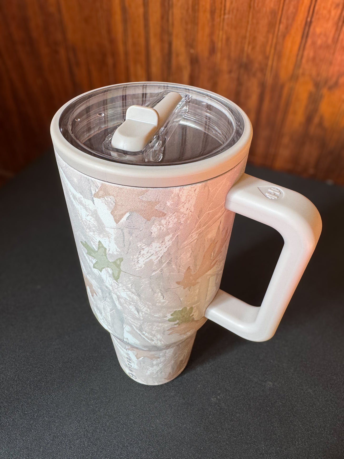 HydroJug 40 oz tumbler in the color camo. Sitting on a black shelf with a wood background.