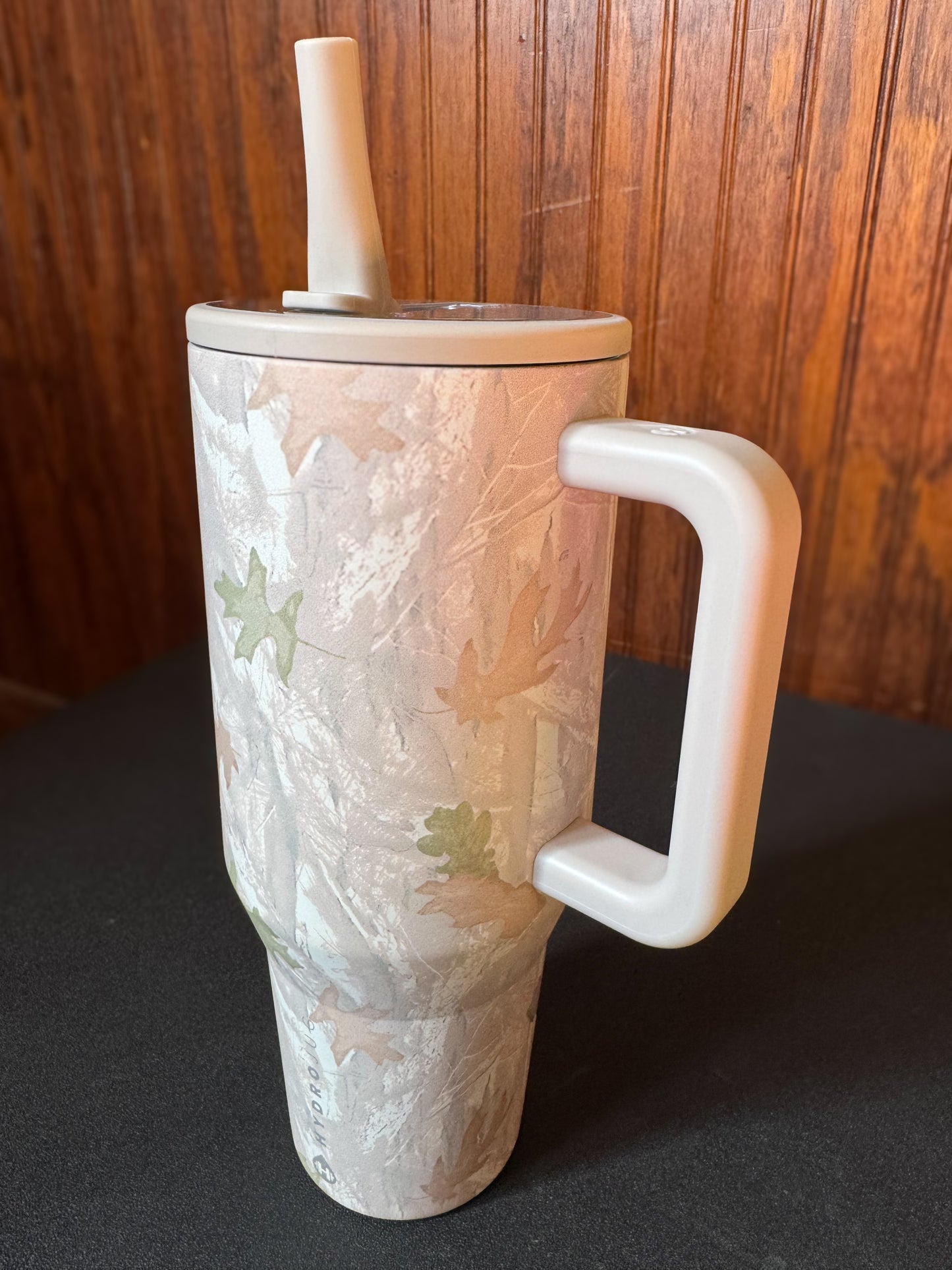 HydroJug 40 oz tumbler in the color camo. Sitting on a black shelf with a wood background.