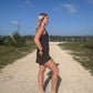 White blonde haired woman wearing a black activewear dress.  She is standing on a dirt road while wearing white vans