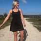 White blonde haired woman wearing a black activewear dress.  She is standing on a dirt road while wearing white vans