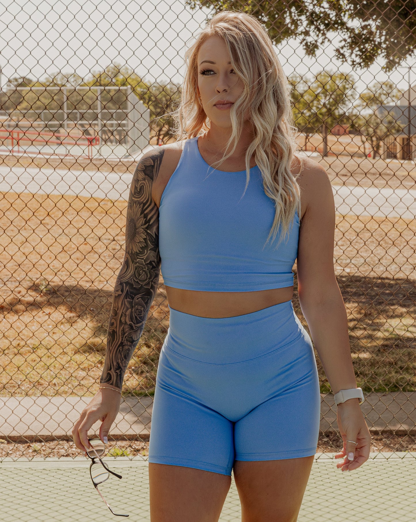 Blonde curly hair women wearing a matching tank top and biker short set in a bright blue color.  She is posing for the camera head on and looking off in the distance.