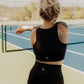 Blonde haired women standing on the middle of a tennis court.  She is facing the opposite direction and is wearing a matching tank top and biker short activewear set.