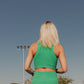 The back side (from the waist up only) of a blonde haired women wearing and matching activewear set.  This includes a long lined tank top with a built in bra and a matching pair of biker shorts both in a bright green color.