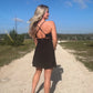 White blonde haired woman wearing a black activewear dress.  She is standing on a dirt road while wearing white vans