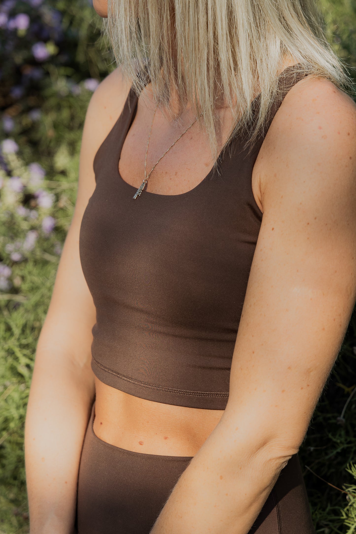 Up close photo of a brown tank top sports bra.  It is being worn by a white women with blonde short hair. 