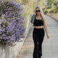 White women with blonde hair wearing a black tank top and flare leggings she is walking down a nature trail area.  She is adjusting the sunglasses on her face.