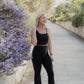 White women with blonde hair wearing a black tank top and flare leggings.  She is messing with her tank top while smiling at someone off the photo.