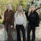 3 white women with all blonde hair standing infront of a concrete wall.  they are all looking in the opposite directions.  They are all wearing the same sweater but in three different colors. 