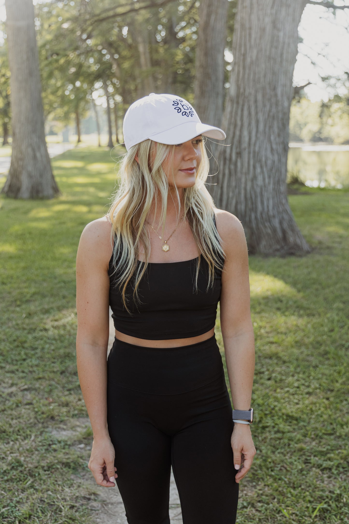 White women with blonde hair wearing a white baseball cap with a logo on the front of it.  