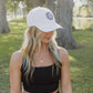 White women with blonde hair wearing a white baseball cap with a logo on the front of it.  