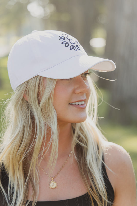 White women with blonde hair wearing a white baseball cap with a logo on the front of it.  