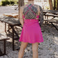 White women with blonde hair wearing it in a messy bun.  She is wearing a pink tennis dress and white van athletic shoes.  She is showing off the back of the dress.  She has visible tattoos on her back as well.