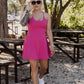 White women with blonde hair wearing it in a messy bun.  She is wearing a pink tennis dress and white van athletic shoes.  She is walking towards the camera with sunglasses on and is starting to pull them off.