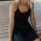 White women with blonde hair sitting on a stage wearing a black tennis dress.  She is looking into the distance.  this photo is mainly taken towards the front.