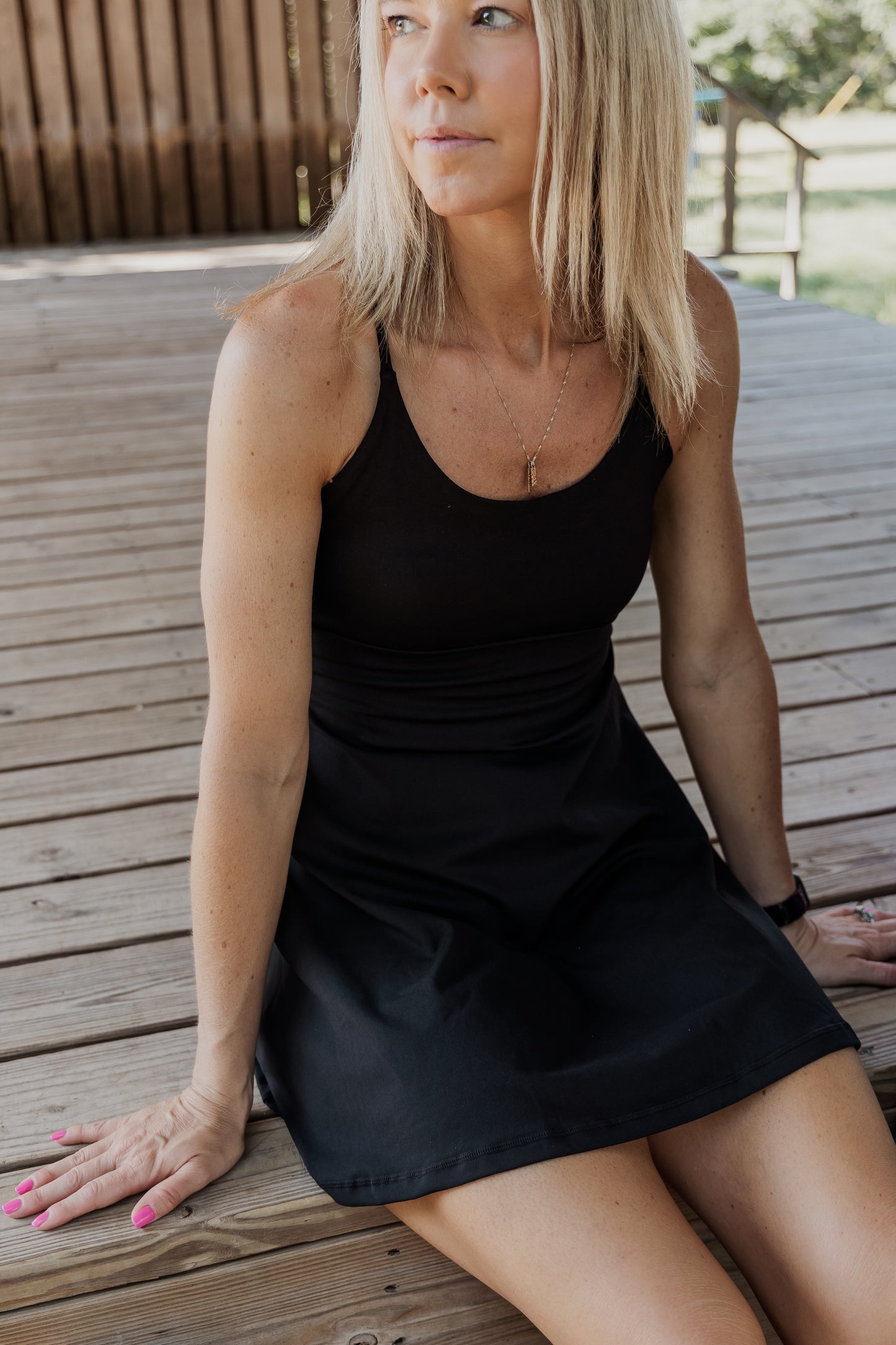 White women with blonde hair sitting on a stage wearing a black tennis dress.  She is looking into the distance.  this photo is mainly taken towards the front.