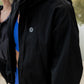 White women with blonde hair wearing a black cropped hooded wind/rain jacket.