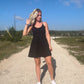 White blonde haired woman wearing a black activewear dress.  She is standing on a dirt road while wearing white vans