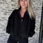 White women with blonde hair wearing a black oversized pullover that is a half zip.  She is standing I. Front a white washed brick wall and has her hands in her pocket. 