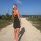 White blonde haired woman wearing a black activewear dress.  She is standing on a dirt road while wearing white vans