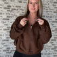 white women wearing an oversized cropped pull over that is a half zip sweater.  She is standing in front of a brick wall