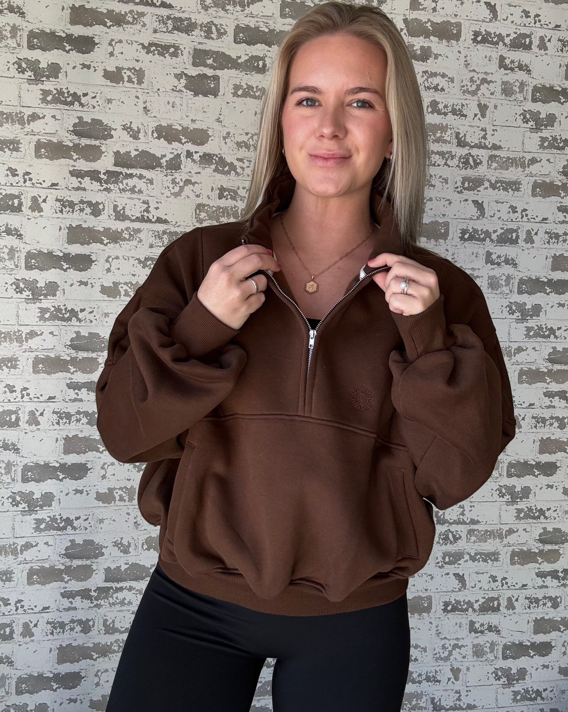 white women wearing an oversized cropped pull over that is a half zip sweater.  She is standing in front of a brick wall