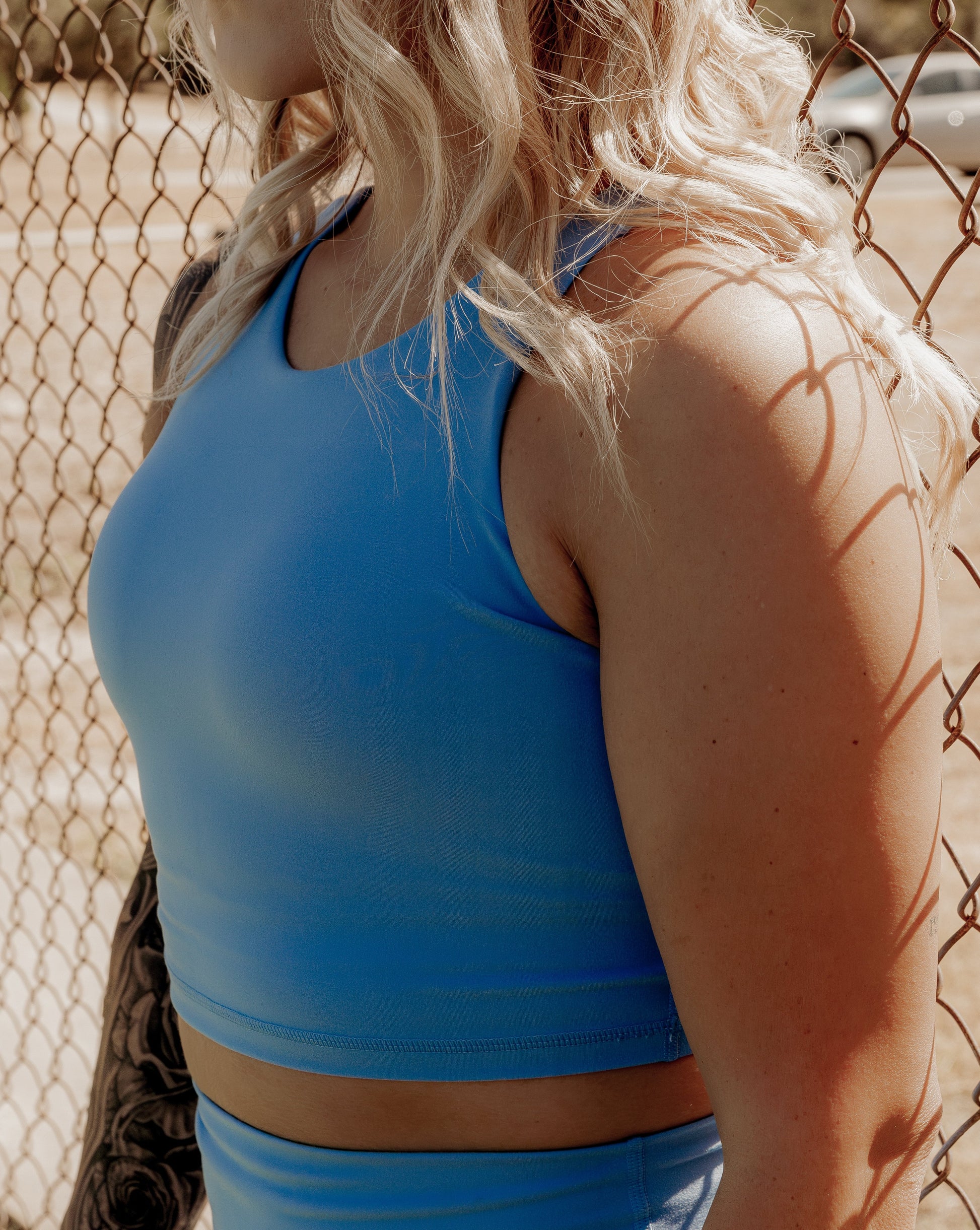 Blonde curly haired women up close on a bright blue tank top that she is wearing.  This photo is to show off the tank top and its features.
