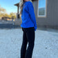 White blonde haired woman wearing a royal blue gilden sweatshirt.  She is looking over her shoulder and showing off the sweatshirt that is pair with a pair of black flare leggings. The sweatshirt has a blue logo embroidered on it with our company logo.