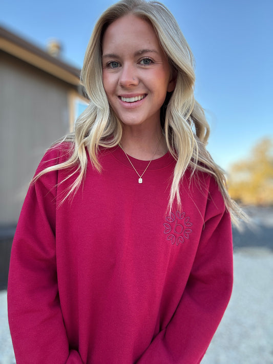 White blonde haired woman wearing a cardinal red gilden sweatshirt.  She is looking straight at the camera and showing off the sweatshirt. The sweatshirt has a red logo embroidered on it with our company logo.