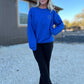 White blonde haired woman wearing a royal blue gilden sweatshirt.  She is looking straight at the camera and showing off the sweatshirt. The sweatshirt has a blue logo embroidered on it with our company logo.