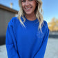 White blonde haired woman wearing a royal blue gilden sweatshirt.  She is looking straight at the camera and showing off the sweatshirt. The sweatshirt has a blue logo embroidered on it with our company logo.