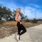 blonde haired white women standing on a dirt road showing off the pockets on her black leggings