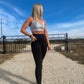 blonde haired white women standing on a dirt road showing off the pockets on her black leggings