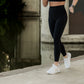 White blonde women with blonde hair running by the water at the park.  she is wearing a black matching leggings and sports bra set and white tennis shoes.