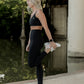 white women with blonde hair stretching her legs by the river at the park.  she is wearing a matching legging and sports bra set in black.  she is wearing white nike tennis shoes.